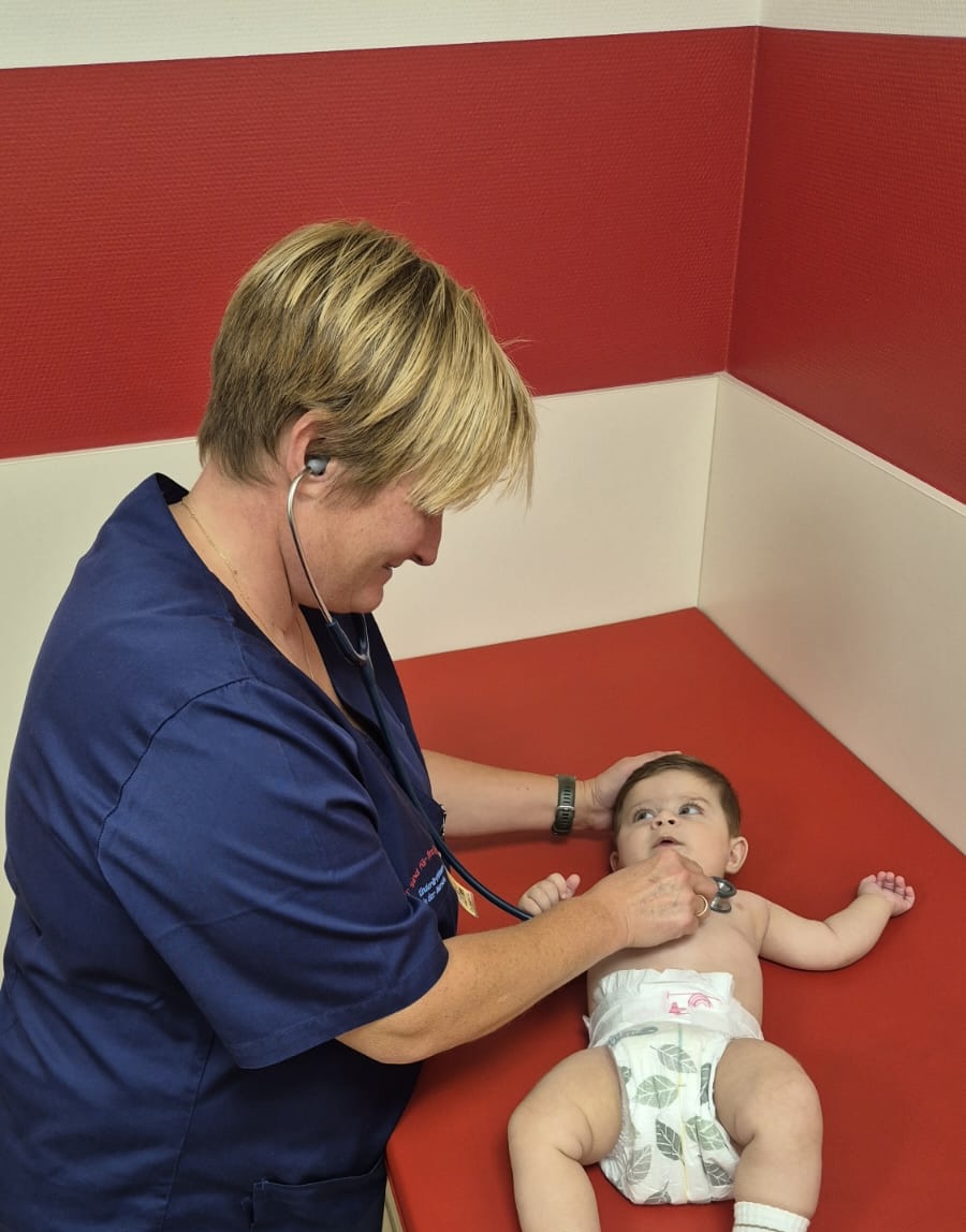 Kinderärztin untersucht ein Baby mit dem Stethoskop auf der roten Untersuchungsliege